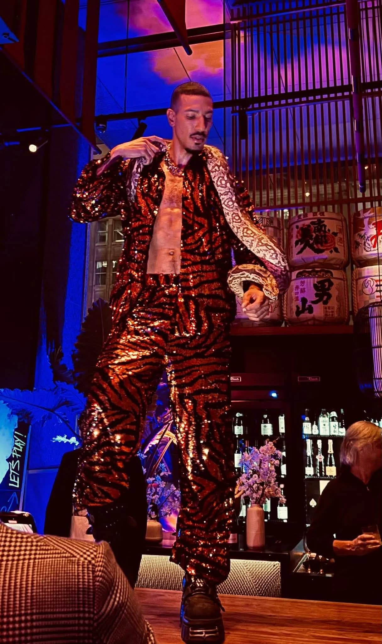 Seth in a sparkly tiger-print suit performing at a nightlife venue with sake barrels in the background